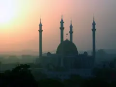 Wschód słońca nad stolicą Nigerii, Abudżą. Monumentalny meczet z kopułą i minaretami wyłania się z porannej mgły.